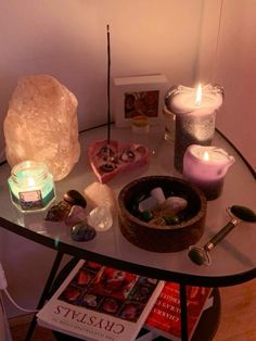 a table topped with candles and rocks on top of a glass table next to a book