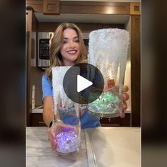 a woman holding two large vases filled with purple and green rocks on top of a counter