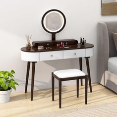 a white desk with a mirror, stool and potted plant on the floor next to it