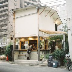 a person standing outside of a small restaurant on the side of a road in front of tall buildings