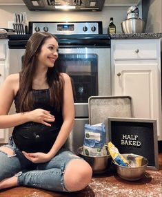 a pregnant woman sitting on the floor in front of an oven with ingredients for baking