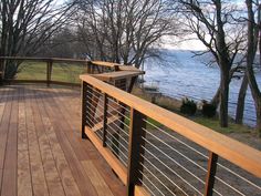 a wooden deck with metal railings next to trees and the water in the background