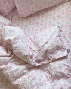 an unmade bed with pink comforters and pillows on top of it, next to a pillow case