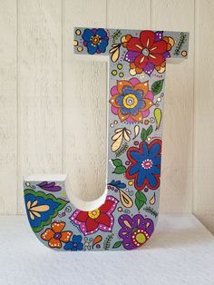 the letter j is painted with colorful flowers and leaves on it's sides,