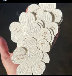 a hand holding a bunch of white coasters with names and numbers on them in front of a black background