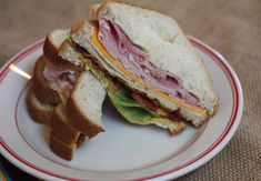 a ham and cheese sandwich cut in half on a white plate with red trim around the edges