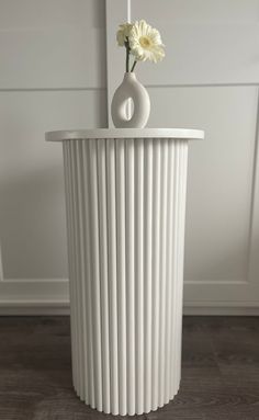 a white vase sitting on top of a wooden floor next to a flower in it