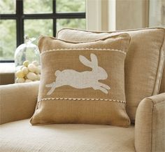 a pillow with a rabbit on it sitting in front of a couch next to a window