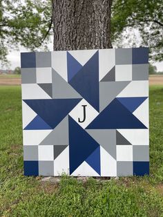 a blue and grey block with the letter j on it in front of a tree