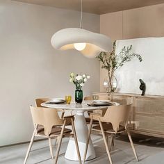 a white table with four chairs around it and a vase filled with flowers on top