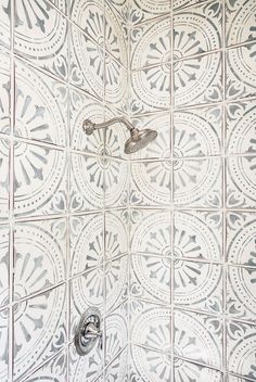 a shower head and hand shower in a white tiled bathroom with silver fixtures on the wall