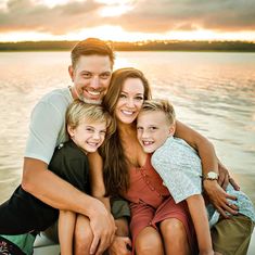 a man, woman and two children sitting on a boat in the water at sunset