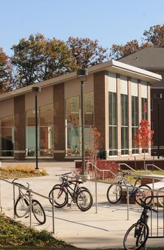 several bicycles are parked in front of a building with glass windows and trees behind them