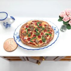 a small pizza sitting on top of a white table next to a vase with pink roses