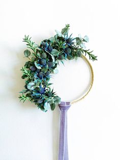 a wreath with blue flowers and greenery hanging on a wall next to a purple tie