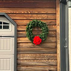 a green wreath on the side of a wooden building with a red rose in it