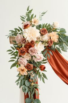 an arrangement of flowers and greenery on top of a wooden cross with red ribbon