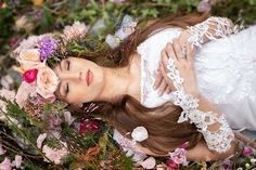 a woman with flowers in her hair is laying on the ground surrounded by greenery