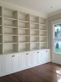 empty white bookcases in the corner of a room with wood floors and windows