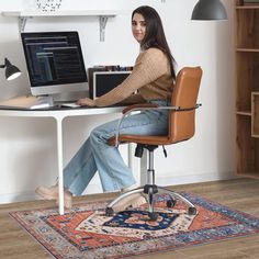 a woman sitting at a desk with a computer on top of it and a rug in front of her