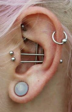 a woman with pink hair has three piercings on her ear and is wearing an ear cuff