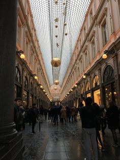 many people are walking through an indoor shopping mall with glass ceiling and lights on the ceiling