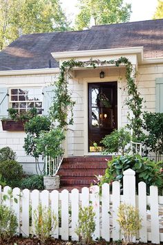 a white picket fence in front of a house with potted plants on the porch