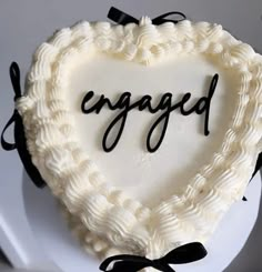 a heart shaped cake with the word engaged written in black lettering on it, sitting on top of a white plate