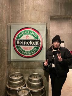 a woman standing in front of keg barrels with her hand up and the sign behind her