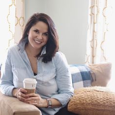 a woman sitting on a couch with a cup of coffee in her hand and smiling at the camera