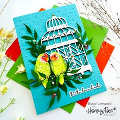 two birds sitting on top of each other in front of a birdcage and flowers