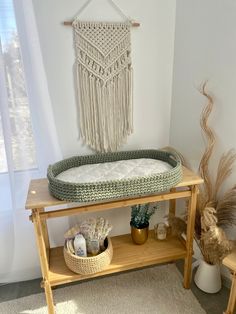 a crocheted baby bed sitting on top of a wooden table next to a potted plant