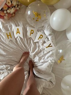 a person laying on top of a bed next to balloons and letters that spell happy