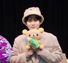 a man holding a teddy bear in front of him and wearing a hat on top of his head