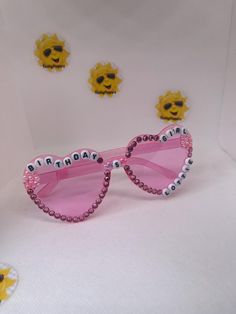 a pair of pink sunglasses with embellishments on the sides and two sunflowers behind them