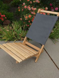 a wooden lawn chair sitting on top of a cement ground next to flowers and bushes