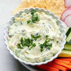 a white bowl filled with dip surrounded by vegetables and crackers