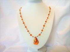 Ref: N025.    This necklace  has amber coloured glass beads, matching seed beads, silvery spacers and an amber coloured dyed shell pendant.  Length is 21 inches and has a sterling silver clasp.  It can be worn on either side one of which is smooth. Amber Beaded Necklace With Large Beads As Gift, Orange Oval Beaded Necklaces As Gifts, Orange Oval Beaded Necklace For Gifting, Orange Oval Beaded Necklace For Gift, Amber Beaded Necklaces With Large Beads For Gifts, Elegant Orange Beaded Crystal Necklace, Amber Beaded Czech Glass Necklaces, Amber Beaded Necklace With Czech Glass, Amber Necklace With Faceted Oval Beads