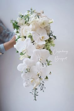 a bridal bouquet with white flowers and greenery is being held by someone's hand