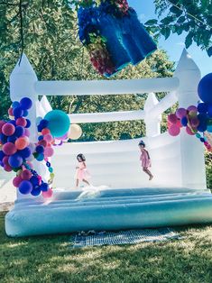 an inflatable castle with balloons and two girls running on the front yard area