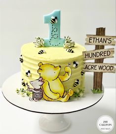 a winnie the pooh birthday cake on a plate with a wooden sign behind it