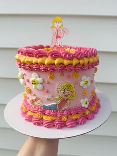 a pink and yellow cake with a cartoon figure on top is being held by a woman's hand