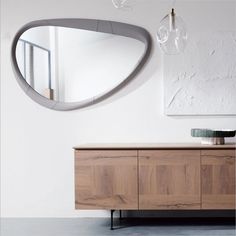 a mirror hanging on the wall next to a wooden cabinet with drawers and cabinets below it