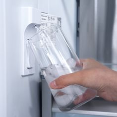 a person is holding a glass in front of the refrigerator door to get something out