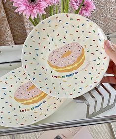 two plates with donuts and sprinkles on them, one being held by a hand