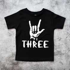 Three Rock on Birthday Shirt, 3rd Rock n Roll Birthday Tee, 3rd Birthday Boy outfit, Three year old Shirt, Born to Rock Theme Please read all the info before placing your order. The price you see is per shirt, please read the size chart in the last pictures of listings before placing your order. How to order a shirt: *Select the STYLE *Select the SIZE *Select the Quantity *Add Personalization *Add to cart *Go back and Repeat for each size (if you need more than one shirt) SHIRTS INFO: *Color: Gr Black Summer Shirt For Birthday, Black Shirt For Summer Birthday, Black Band Merch T-shirt For Birthday, Birthday Band Merch Tops With Short Sleeves, Short Sleeve Band Merch Tops For Birthday, Band Merch Tops For Birthday With Short Sleeves, Three Year Old Birthday Party Boy, 3 Year Birthday Theme Boy, Rock N Roll Birthday