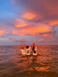 two people standing in the water with their arms up and one person sitting on top of them