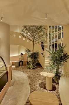 a person sitting on a bench near a tree in a room with stairs and plants