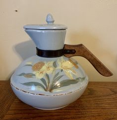 a white vase with yellow flowers painted on the side and a wooden handle sitting on a table