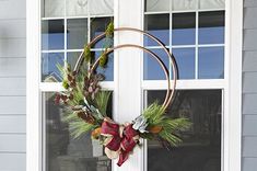 a wreath hanging on the front door of a house with evergreens and plaid bows